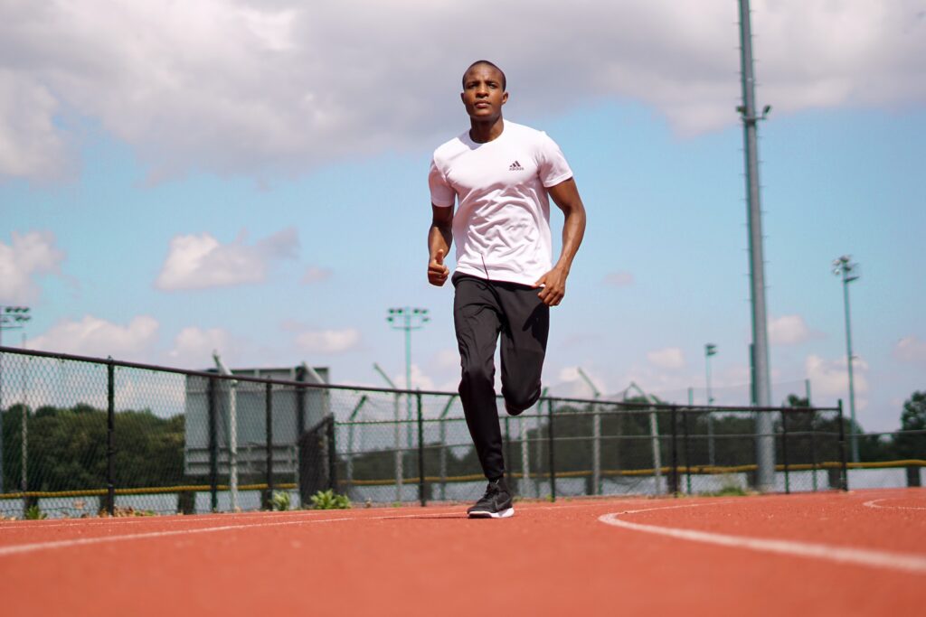 man in white crew neck t-shirt and black pants standing on track field during daytime