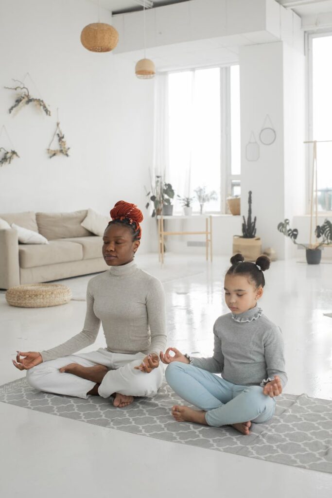 Calm African American woman with daughter meditating with closed eyes in living room